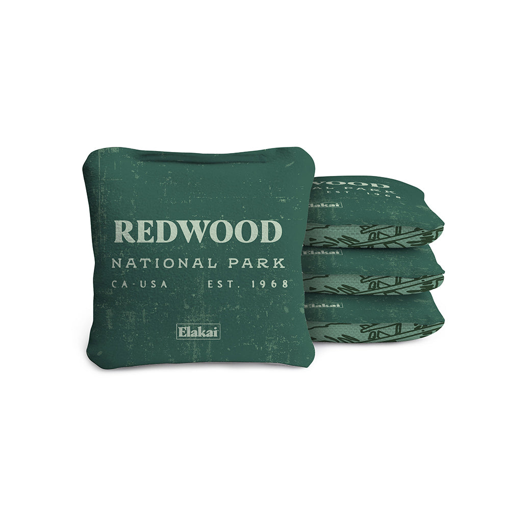 #color_green A set of four green travel-size cornhole bags with 'REDWOOD NATIONAL PARK, CA' printed on them and the brand 'ELAKAI' displayed.