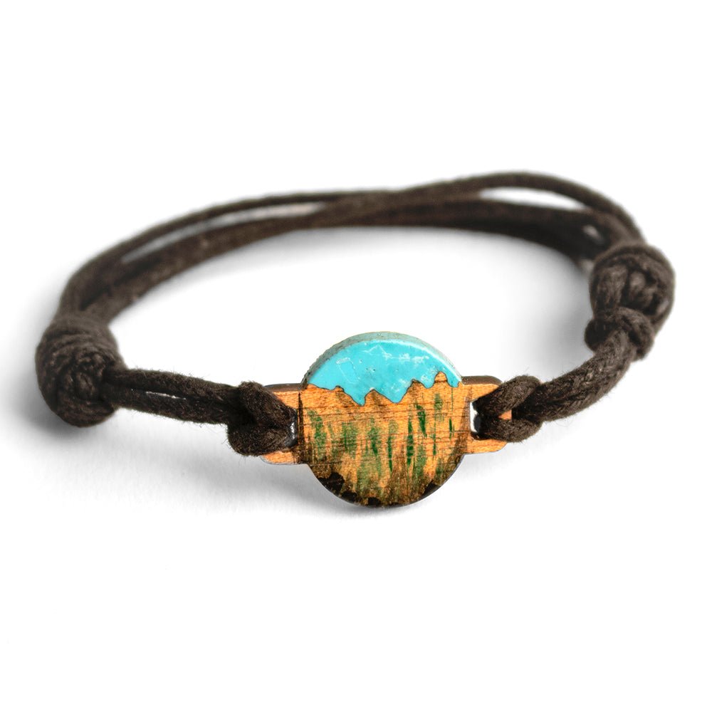 #color_blue turquoise sky wood A bracelet with a resin painted wood scene set in the center, attached to a dark waxed cord.