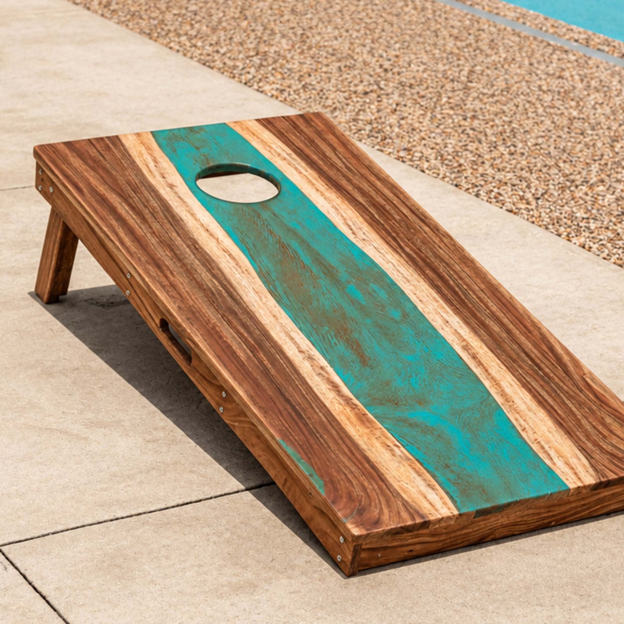 A wooden cornhole board set outdoors on a patio beside a pool, with a turquoise and natural wood grain design and a circular hole near the top. #color_teal and orange