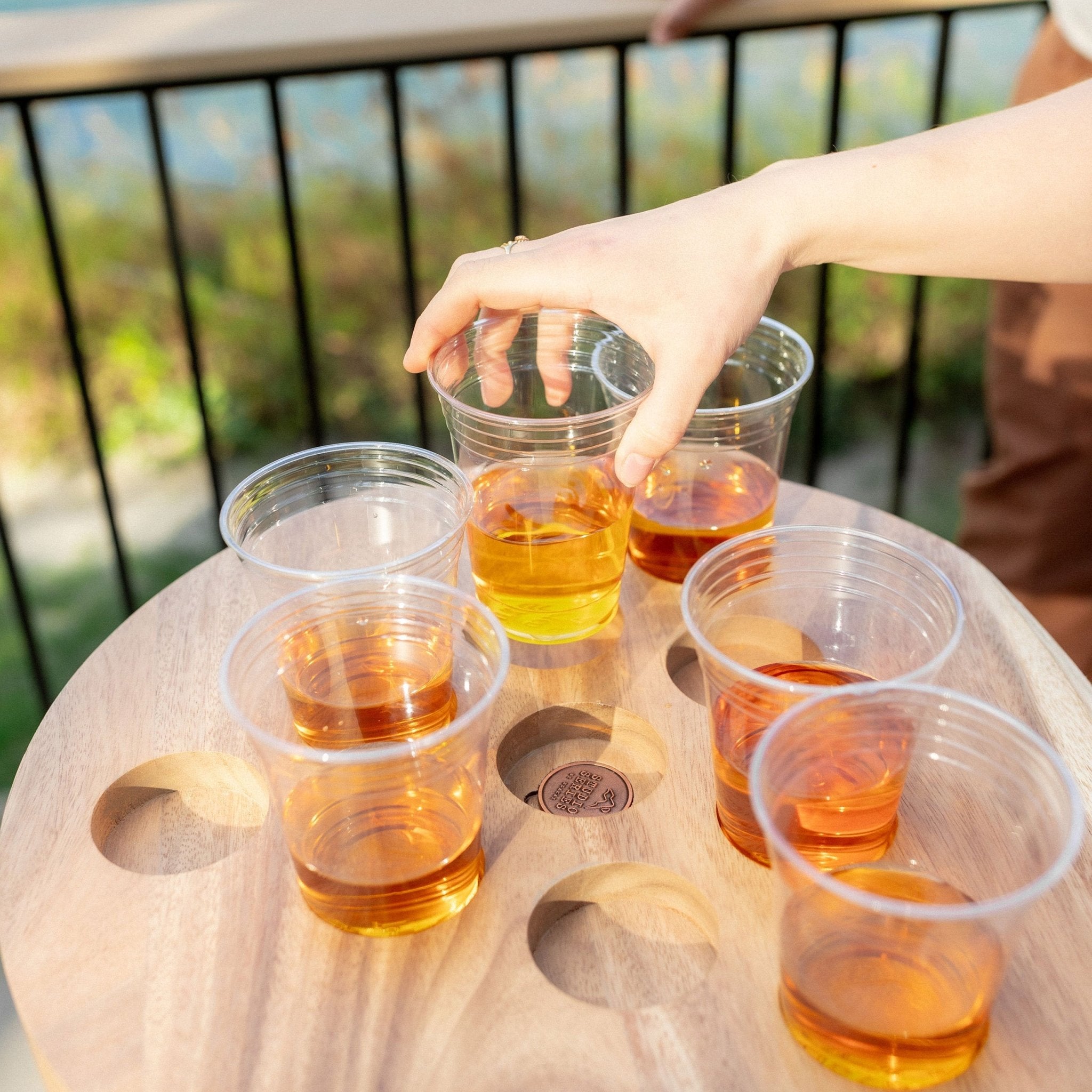 A hand lifting a cup from a carved recess in the live edge acacia Social Pong tabletop