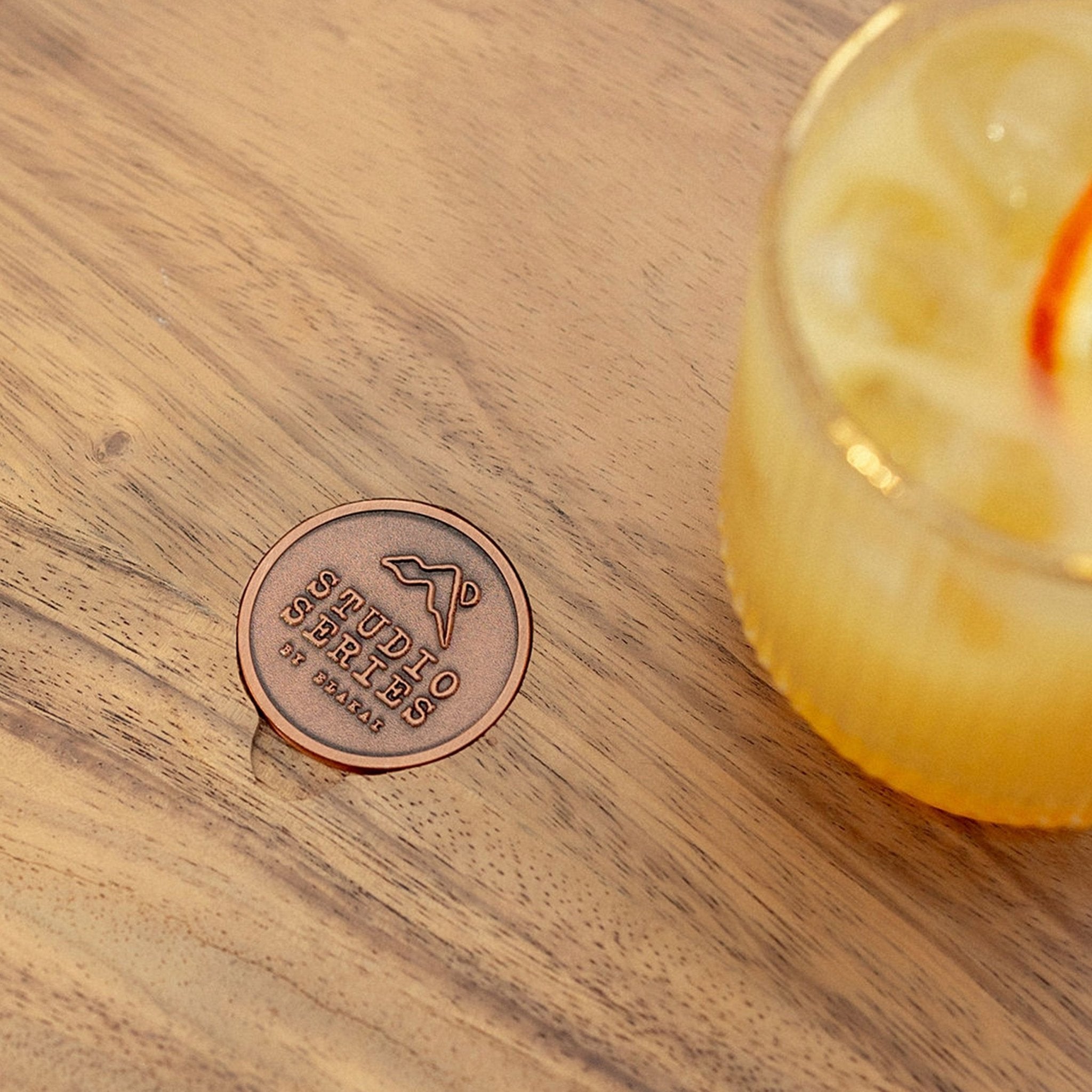 Copper Studio Series medallion set into the acacia accent tabletop beside a whiskey sour cocktail