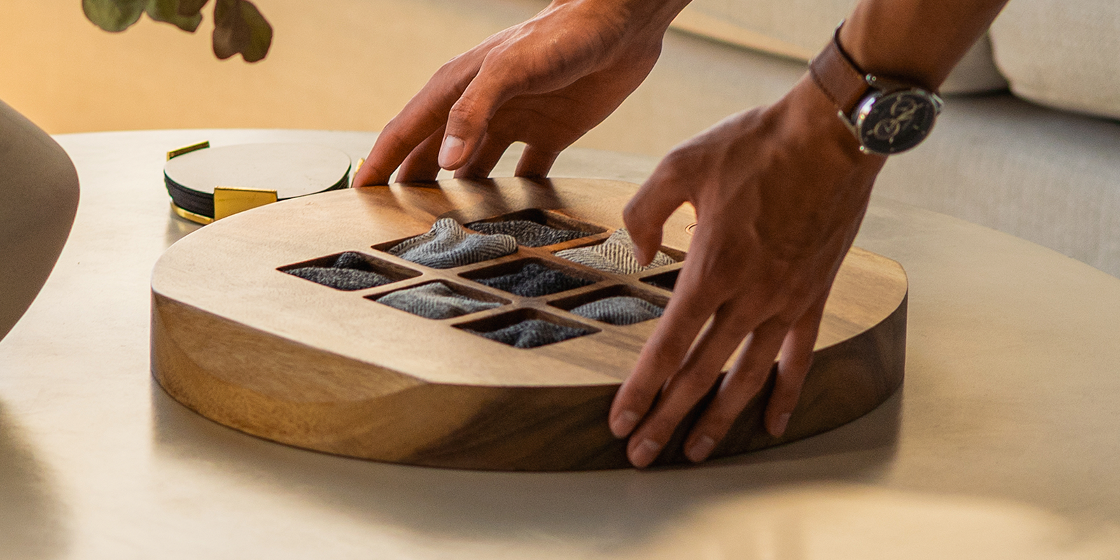 Hands placing the Studio Series Tic Tac Toe game on a modern coffee table.