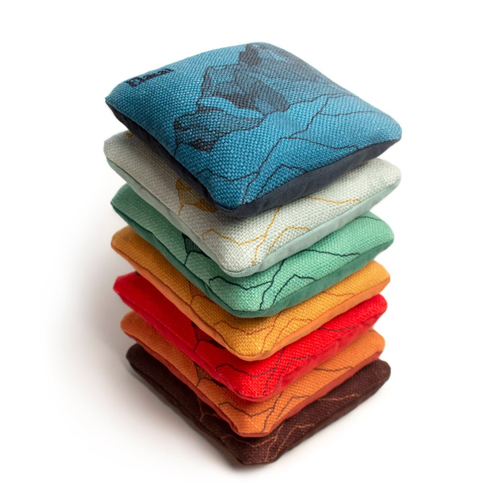 A stack of six cornhole bags in various colors, featuring a dual-sided design with one smooth and one grip side.