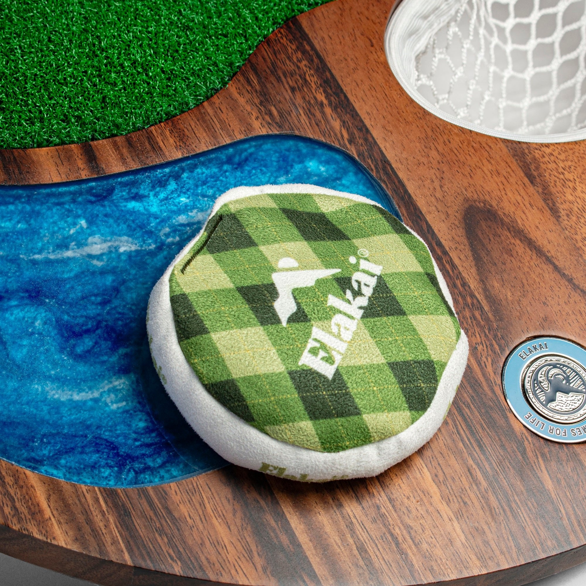 Green checkered Elakat product on a wooden surface with grass and water background