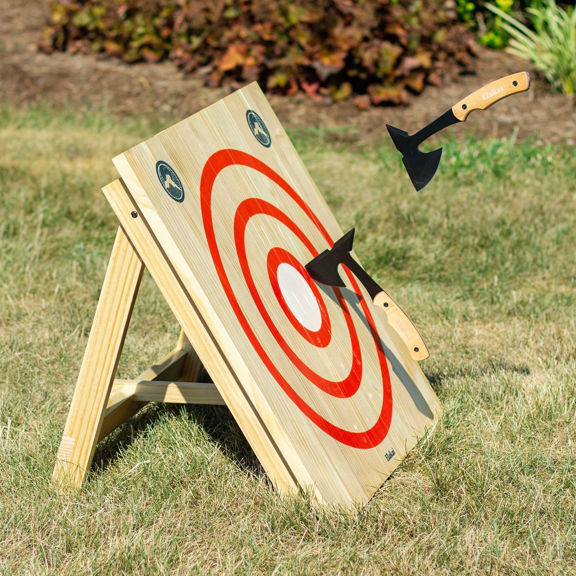 Wooden target board with red and white design, placed outdoors on grass.