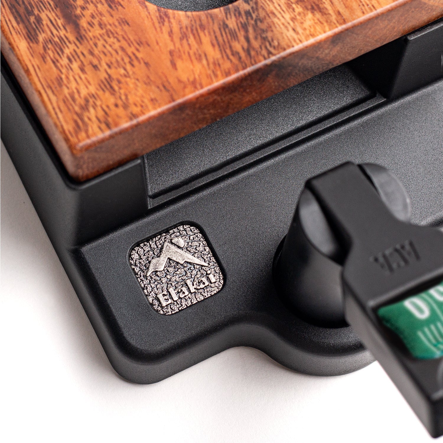 Close-up detail of the Elakai Gameday tabletop mini double chuck cornhole game showing textured metal Elakai badge on black base with wood and resin construction