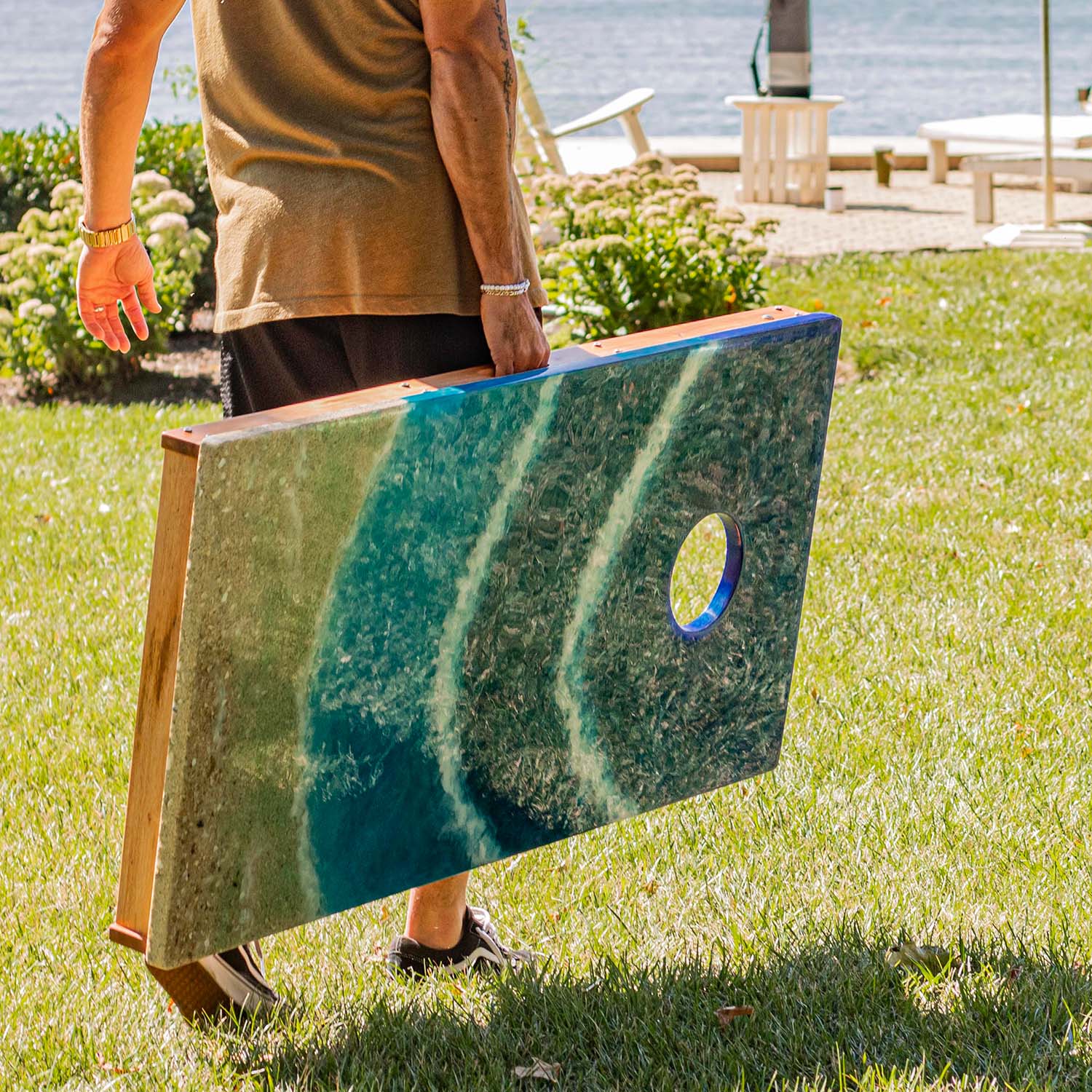 Person carrying a lightweight Elakai beach resin cornhole board across the lawn