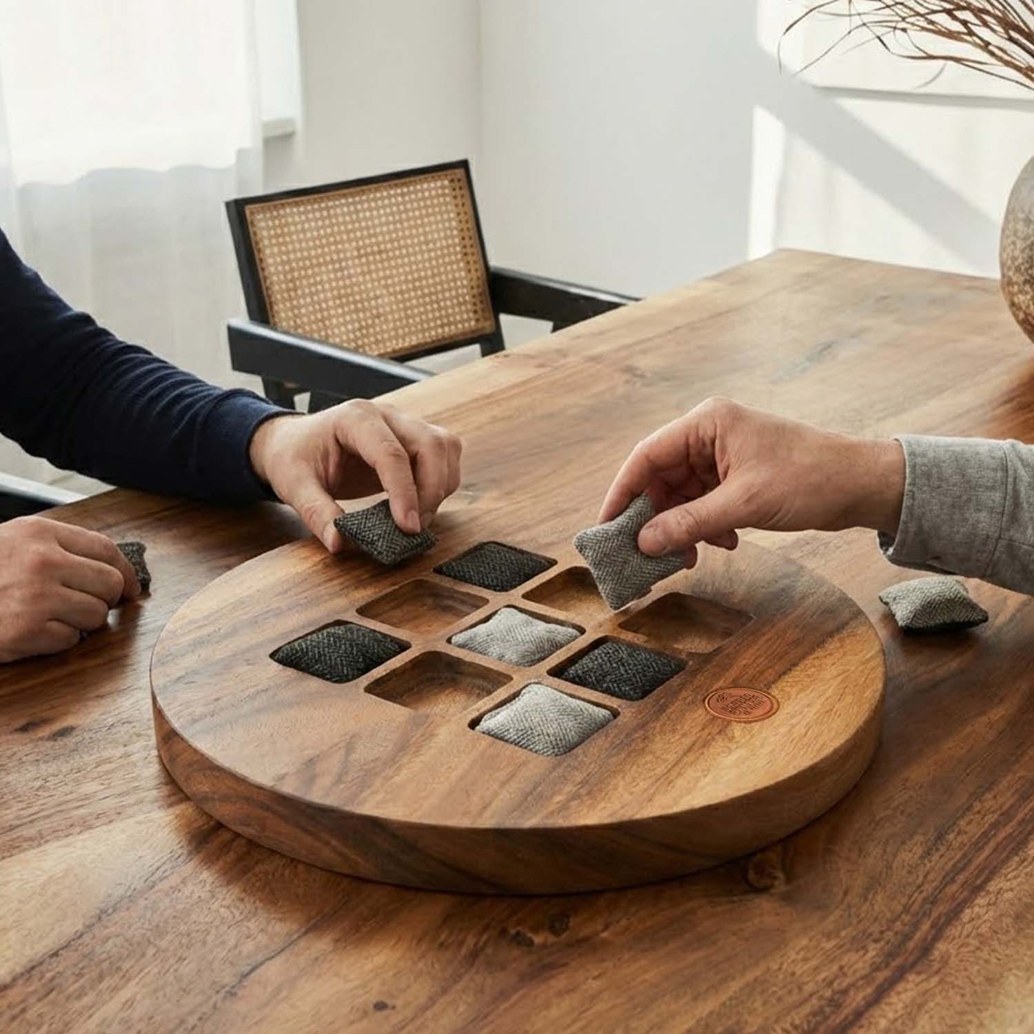 Two people playing a modern acacia wood tic tac toe game with soft herringbone wool pieces on a wooden table