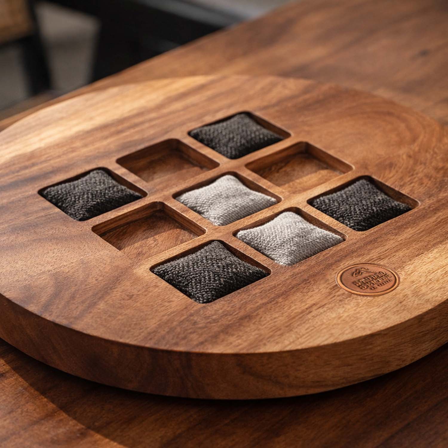 Macro view of herringbone wool tic tac toe game pieces resting on an acacia wood board showing fabric texture and wood grain