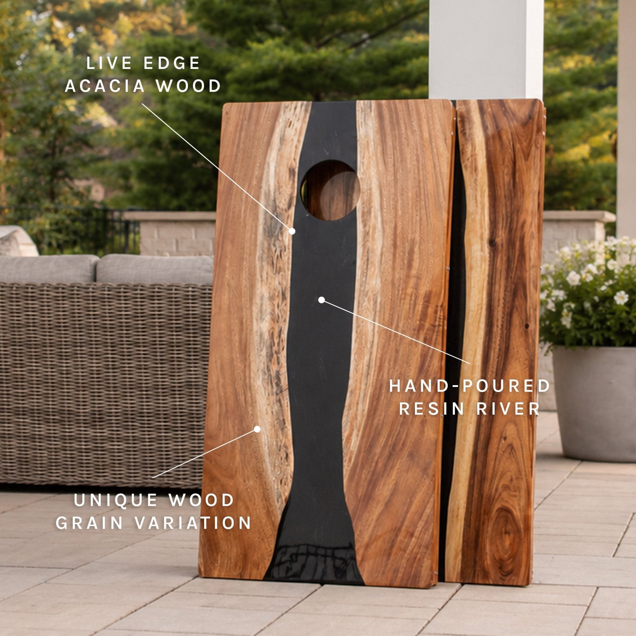 A wooden cornhole board with a live edge acacia wood finish and a black hand-poured resin river, shown outdoors on a patio with text callouts highlighting the materials. #color_black