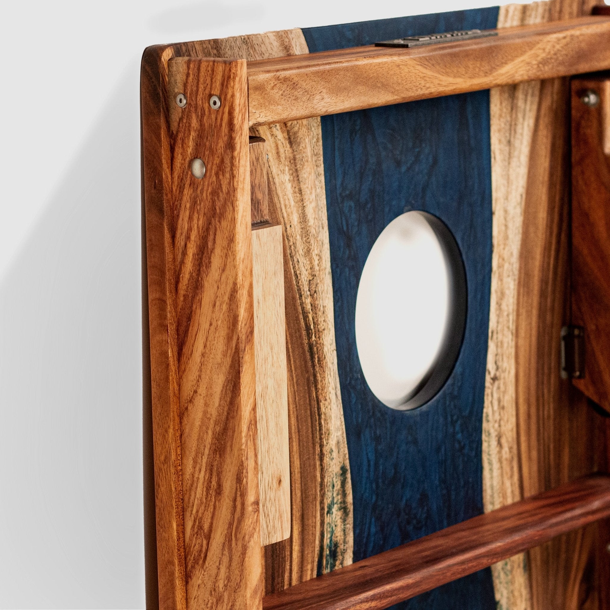 Close-up of a wooden wall-mounted shelf or cabinet panel with a circular cutout, featuring natural wood grain, a dark blue inlay, and visible metal screws and hinges. #color_blue pearl