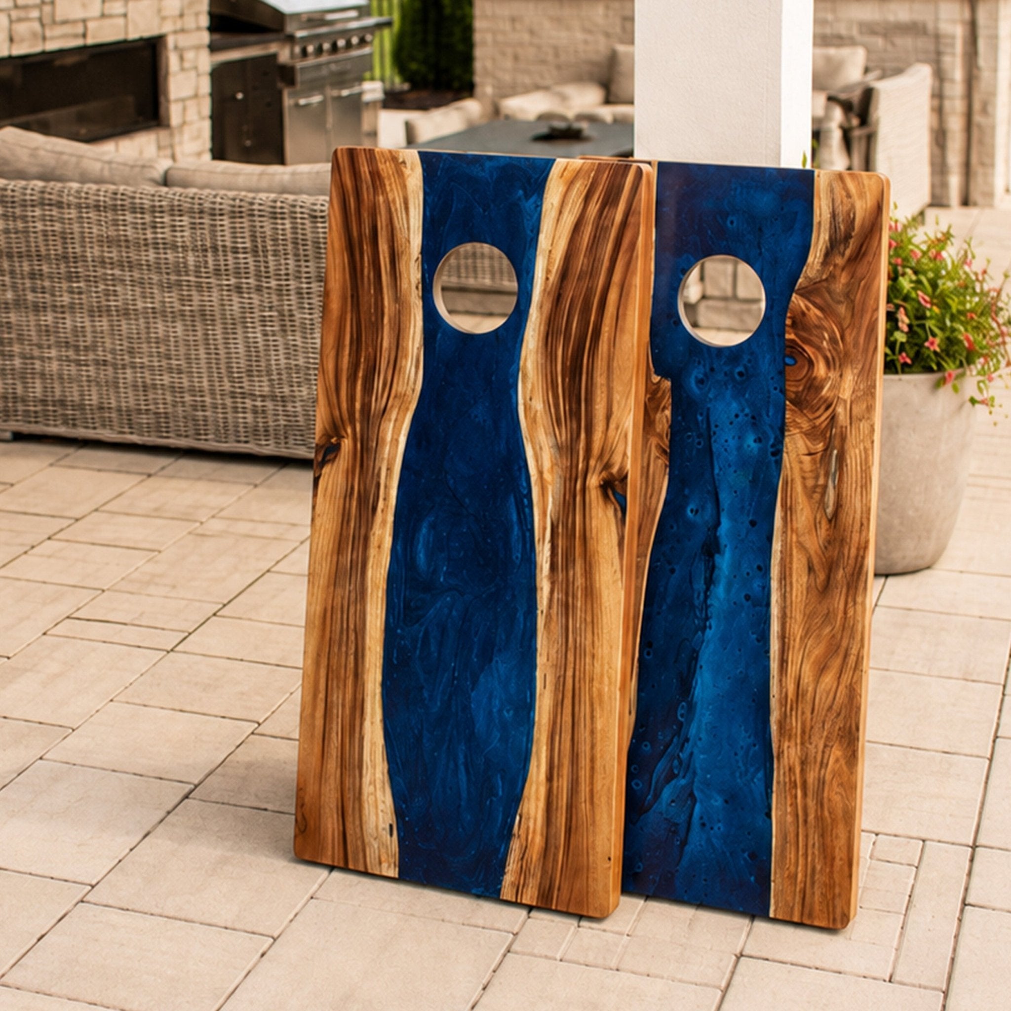 Two wooden board game boards with a blue resin inlay and live-edge wood sides, displayed on a tiled patio in an outdoor living room setting. #color_blue pearl