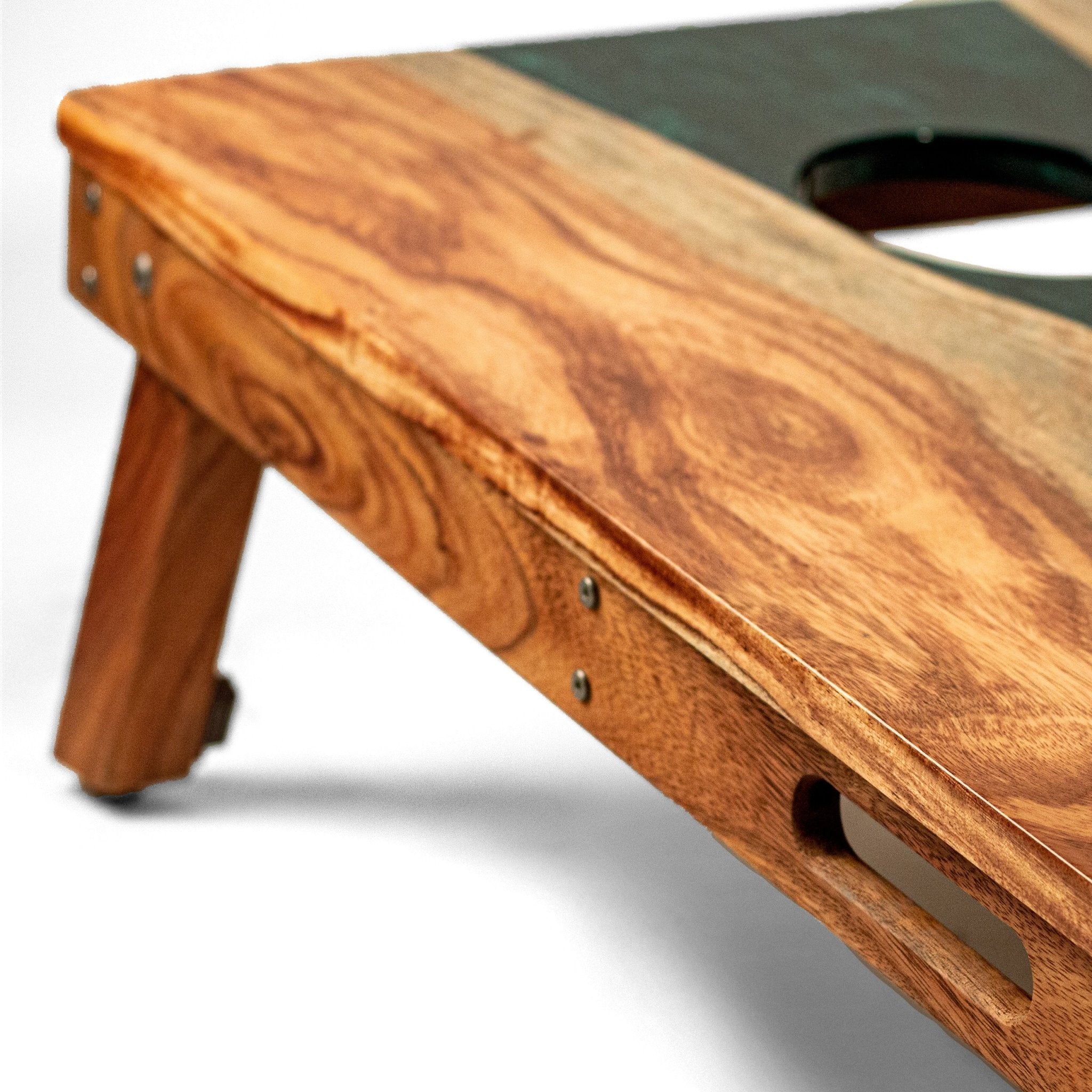 Close-up of a wooden cornhole board showing the natural wood grain, metal hardware, and a dark playing surface with a hole. #color_green pearl