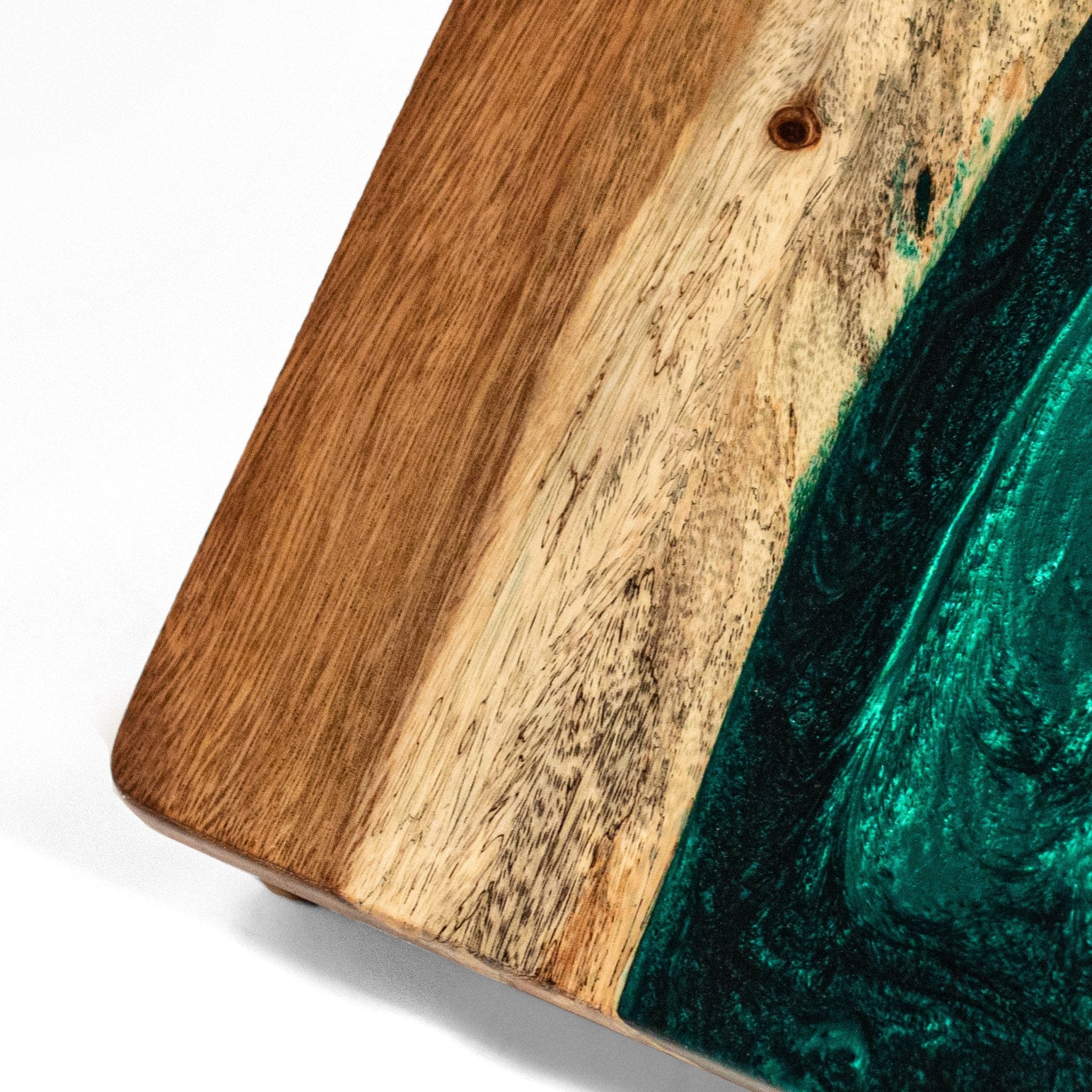 A close-up of a wooden board or tray corner showing a natural wood grain surface with a dark green resin inlay on a white background. #color_green pearl
