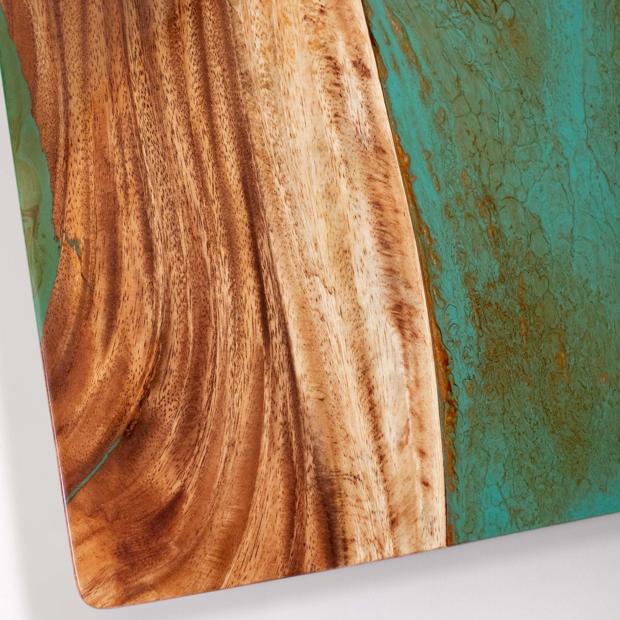A close-up of a cornhole board featuring a split design: one side shows warm brown wood grain, and the other side has a textured turquoise-green surface with gold veining. #color_teal and orange