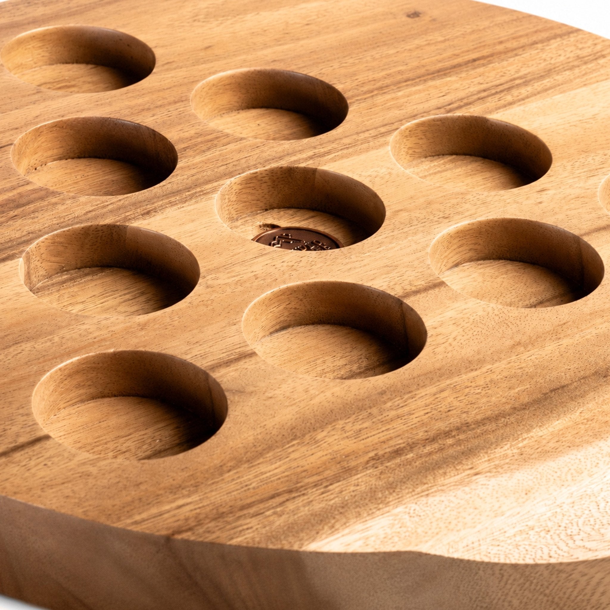 Ten hand-carved cup recesses in the solid acacia Social Pong tabletop, arranged in a triangle around a copper medallion